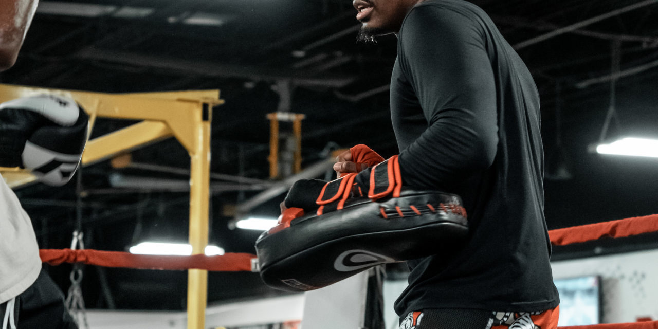 Male Muay Thai trainer holding pads during a training session.