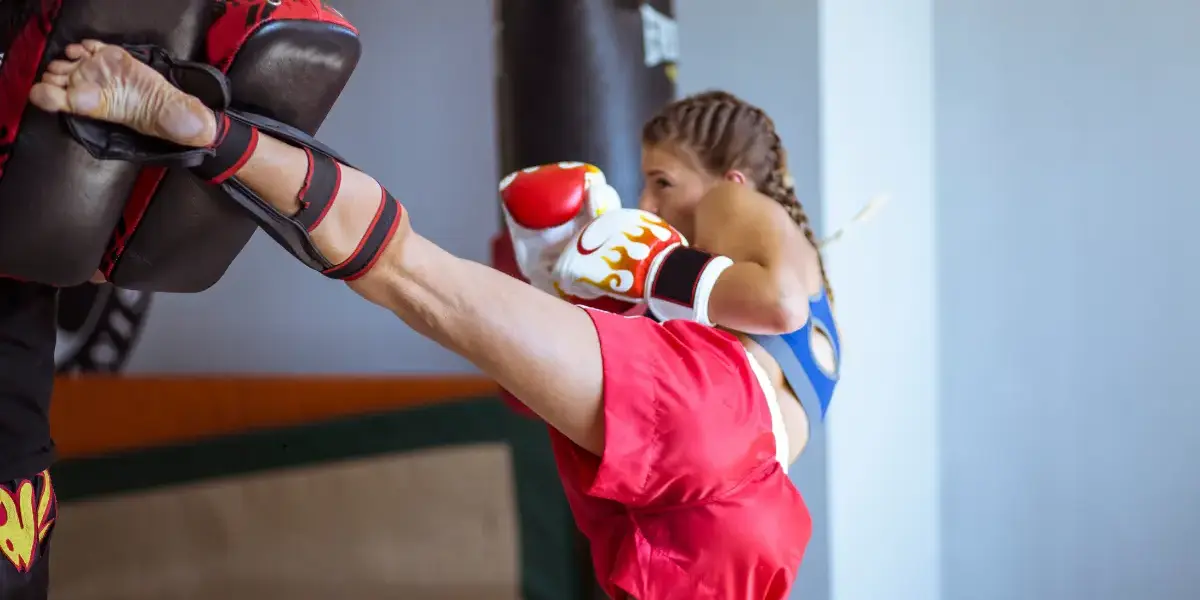 Female kickboxer delivering a high kick to a padded target during training