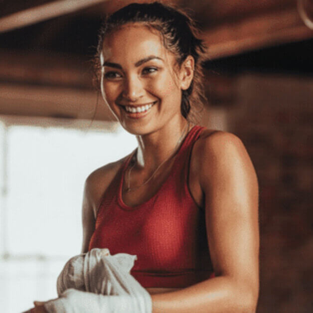 Smiling Woman Post-Workout Smiling woman in a red sports top wrapping her hands in a gym.